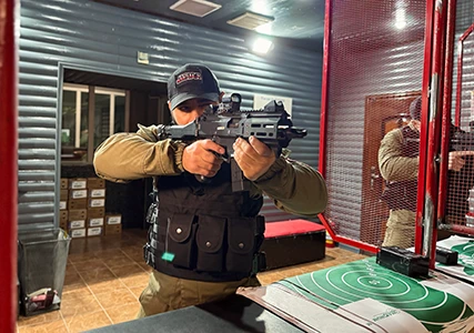 Сотрудник службы безопасности в бронежилете и маске с автоматом в руках на фоне офисного помещения